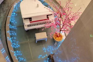 A room with a piano, a bench, and a decorative tree.