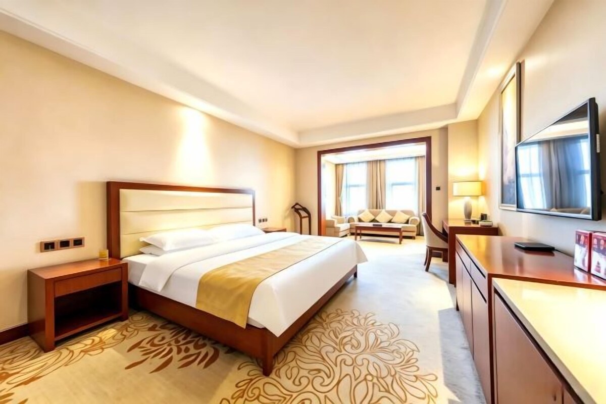 Une chambre d’hôtel avec un grand lit, des tables de chevet, un bureau, une chaise, une télévision et une fenêtre.