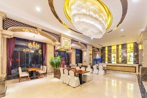 Um saguão de hotel com um lustre, área de estar, balcão de recepção e amplas janelas.