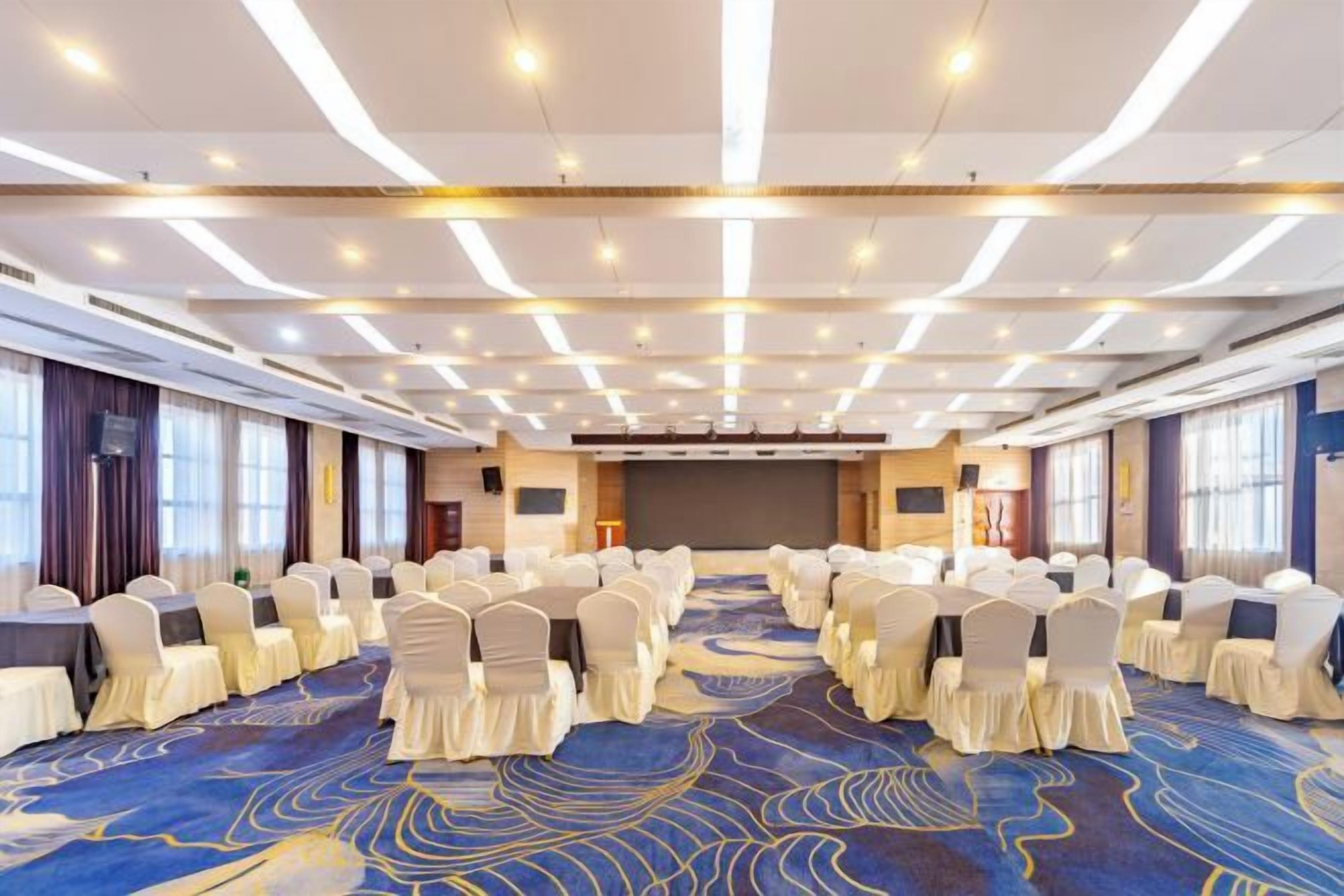 Un salón de conferencias con filas de sillas, un escenario y suelo alfombrado.
