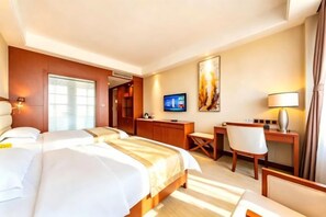 A hotel room with two beds, a desk, a chair, a television, and a painting on the wall.