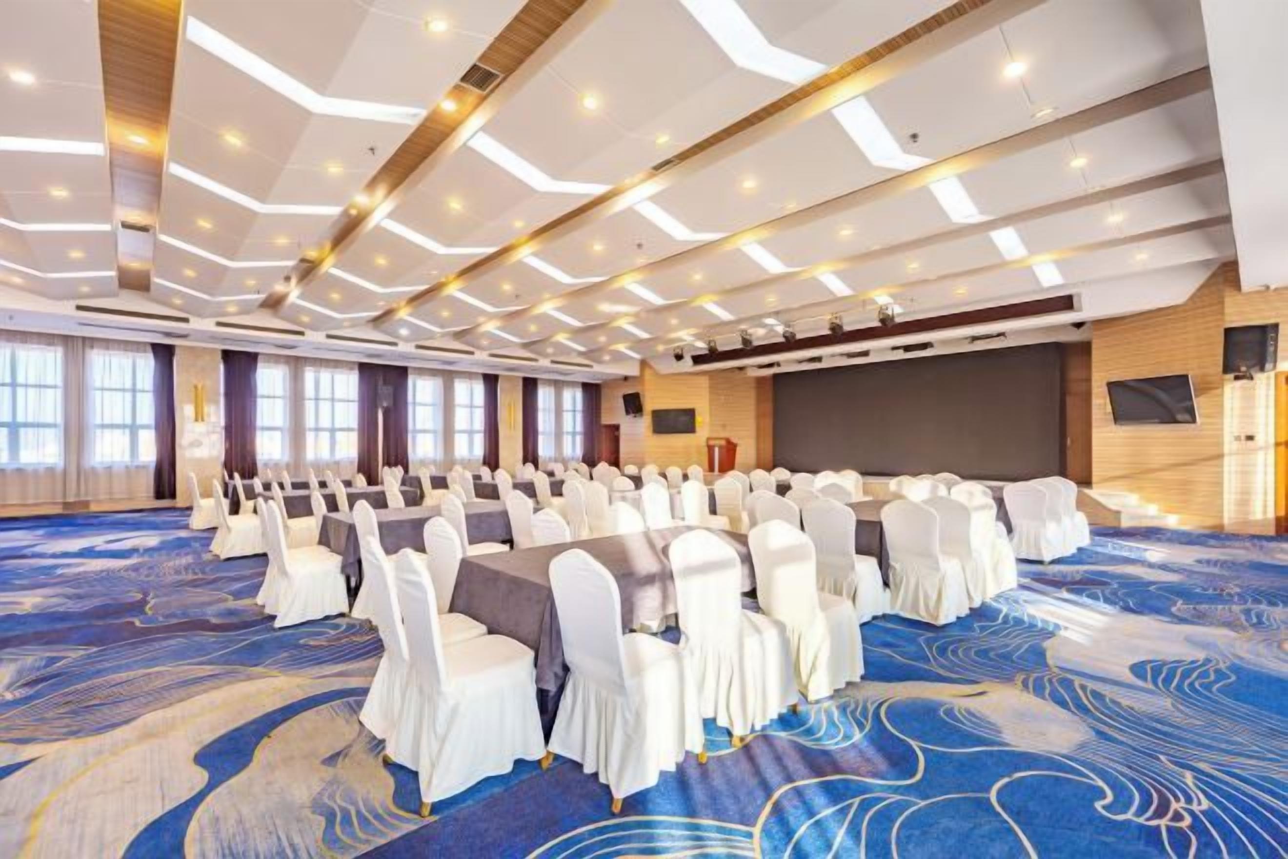 A conference room with rows of chairs, a stage, and a large screen.