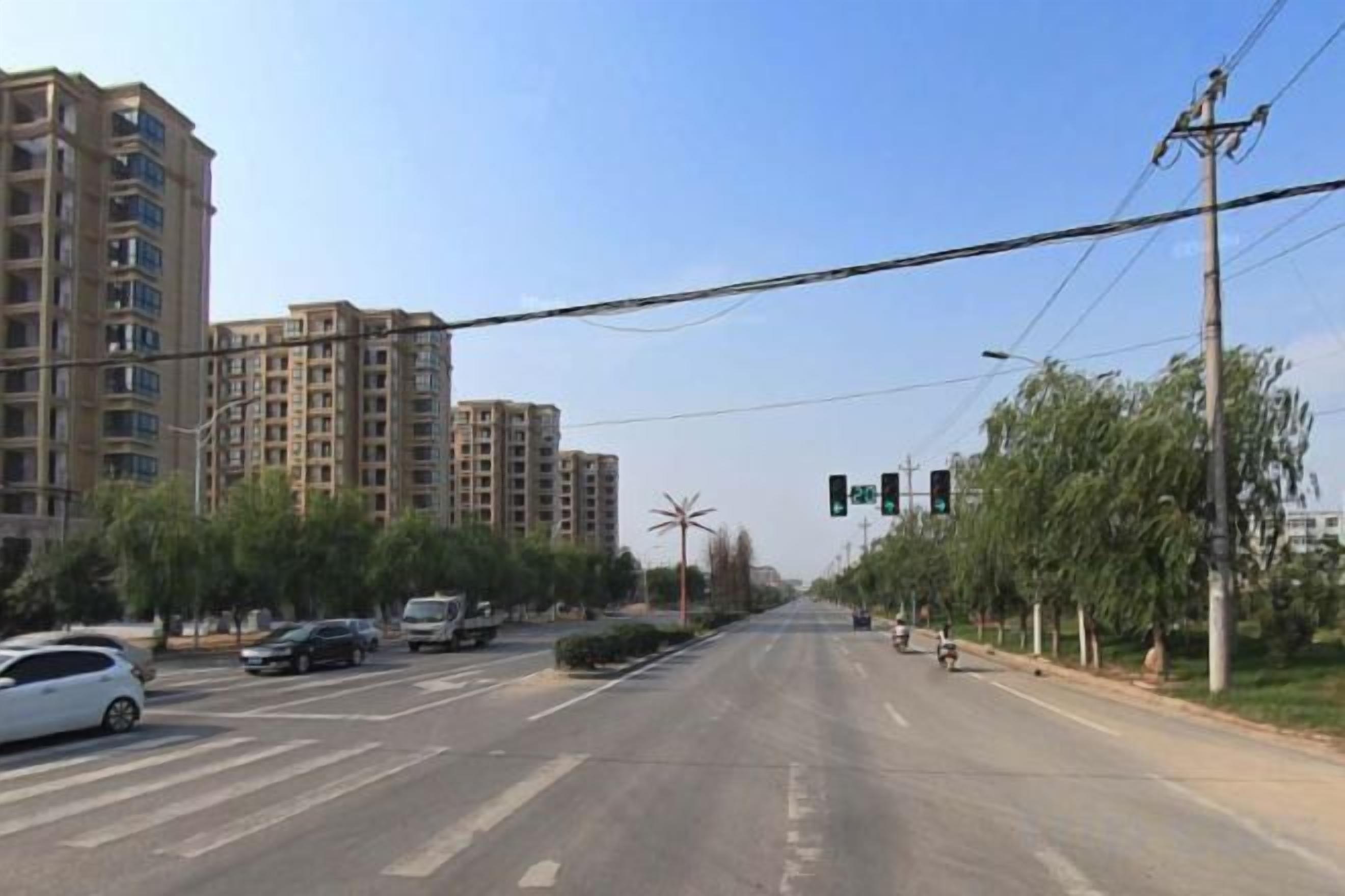 A multi-lane road with traffic lights, vehicles, and buildings in the background.