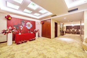 A hotel conference room with a red table, floral decorations, a large window, and a door leading to another room.