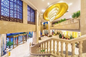 Um hall espaçoso com uma escadaria imponente, painéis decorativos e um lustre.