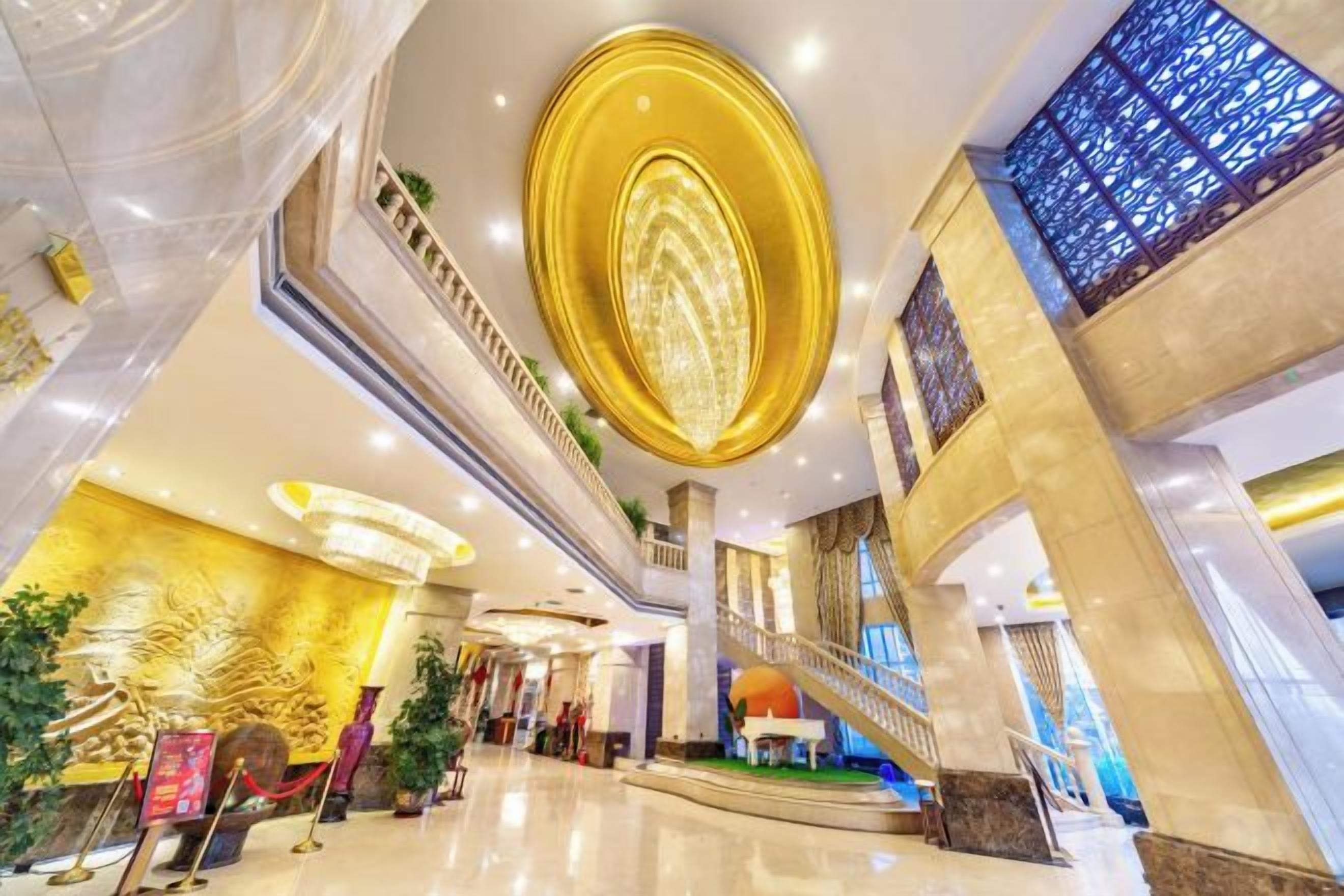 A spacious lobby with a grand staircase, a large chandelier, and a high ceiling.