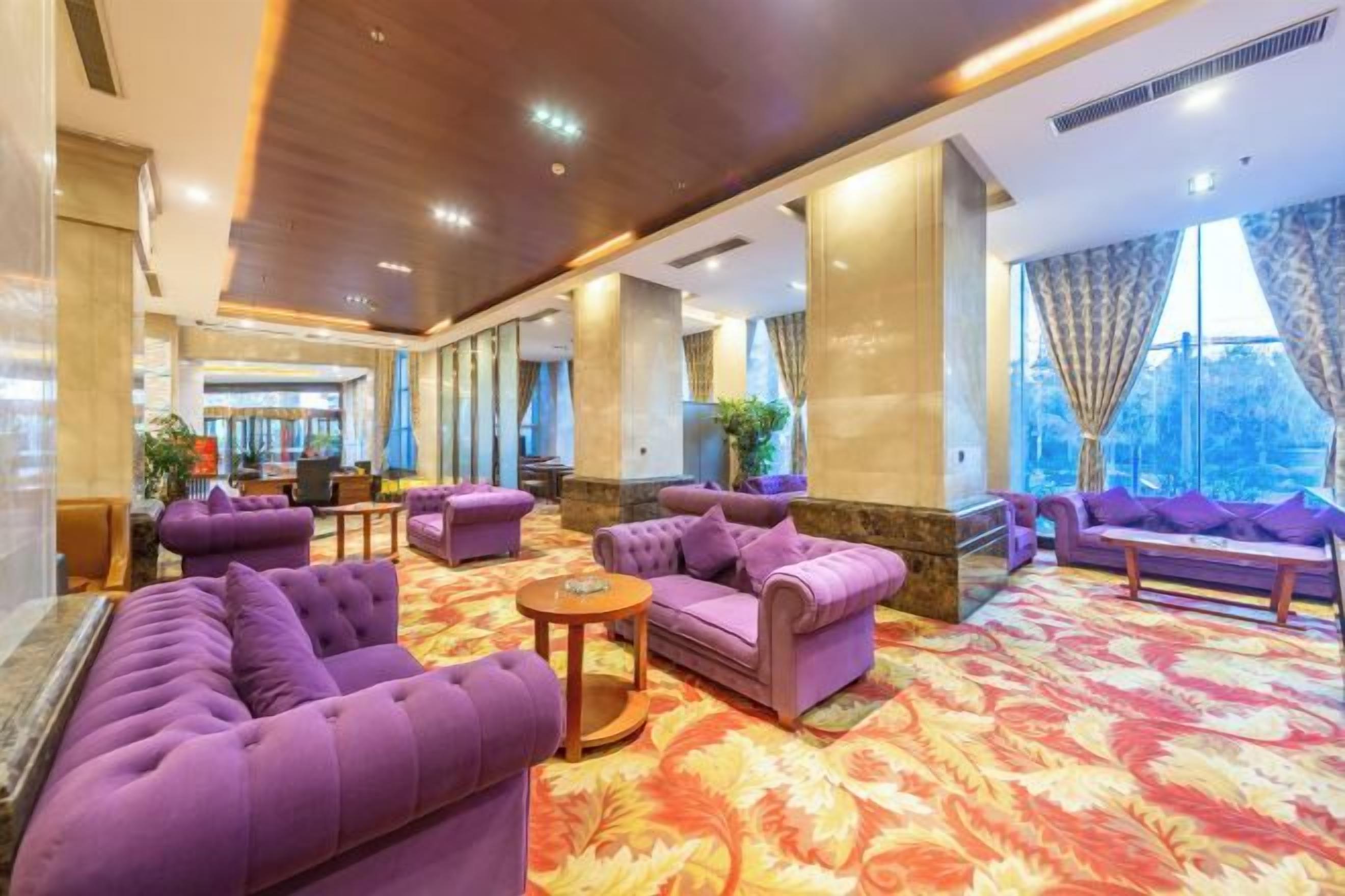 A lobby with purple sofas, a patterned carpet, and large windows.