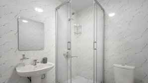 Um banheiro moderno com chuveiro em cabine de vidro, pia em pedestal e vaso sanitário.