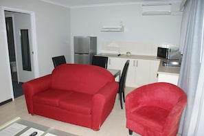 A compact kitchenette with a refrigerator, microwave, and a small dining area with a red sofa and chairs. - Apollo Bay Motel & Apartments (Apollo Bay)