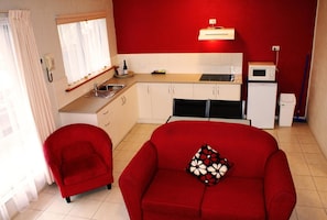 A compact living space with a kitchenette, a red sofa, a red armchair, and a window with curtains. - Apollo Bay Motel & Apartments (Apollo Bay)