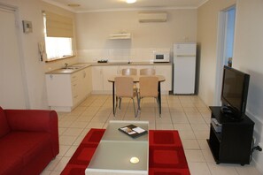A compact living space with a kitchenette, a dining area, a red sofa, and a television. - Apollo Bay Motel & Apartments (Apollo Bay)
