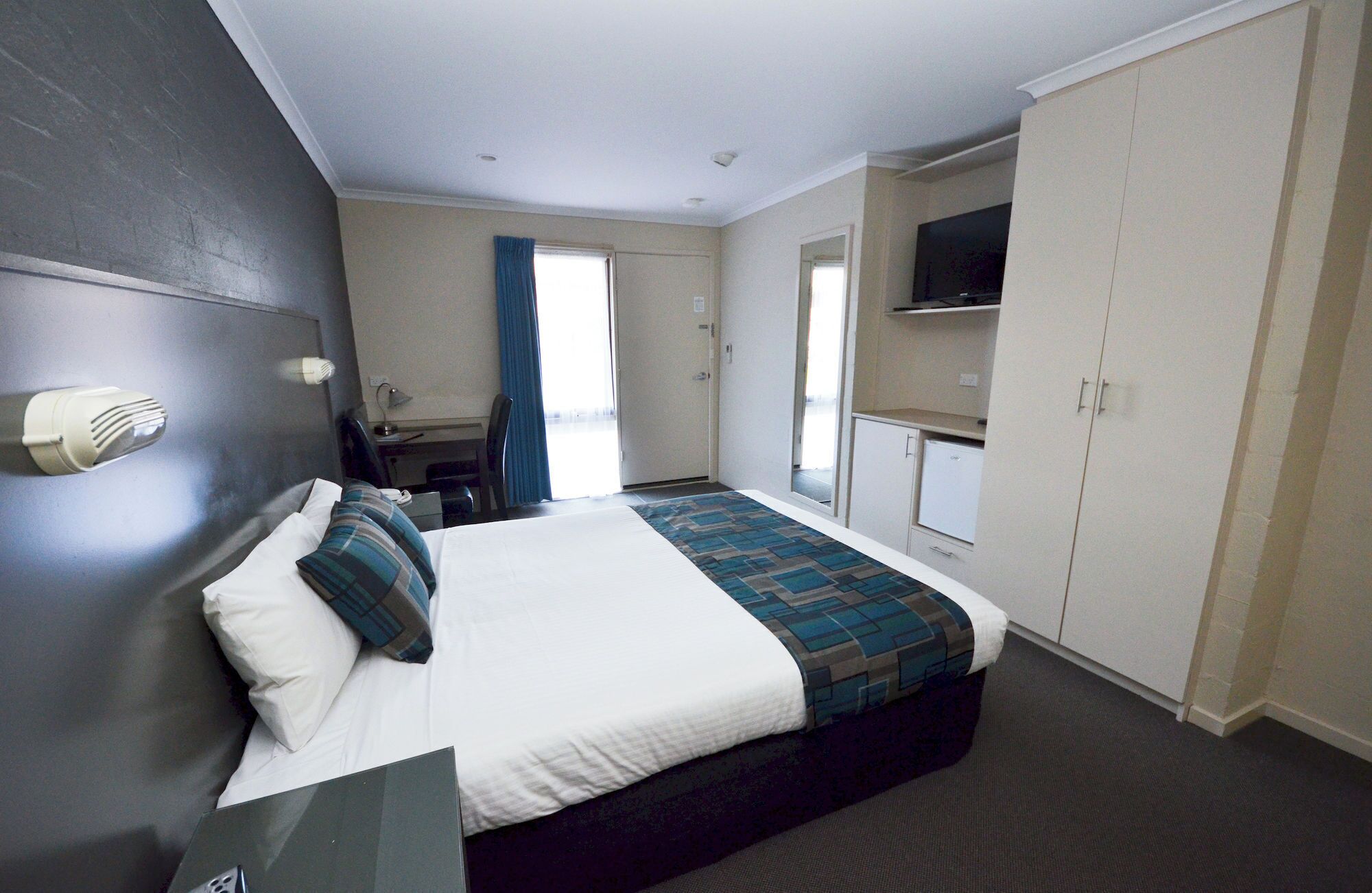 A hotel room with a bed, a desk, a chair, a television, and a wardrobe.