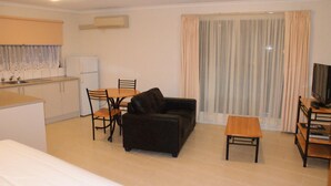 A compact living space with a kitchenette, a sofa, a small table, and a television. - Apollo Bay Motel & Apartments (Apollo Bay)