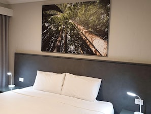 A hotel room with a bed, a nightstand, a wall-mounted lamp, and a large nature-themed picture above the bed. - Apollo Bay Motel & Apartments (Apollo Bay)