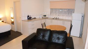 A compact hotel room with a kitchenette, a bed, a black leather sofa, and a dining table.