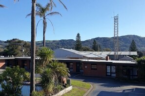 A building with a flat roof, a parking area, and a view of hills. - Apollo Bay Motel & Apartments (Apollo Bay)
