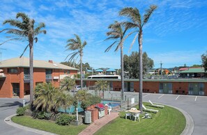 A residential area with a swimming pool, palm trees, and a brick building. - Apollo Bay Motel & Apartments (Apollo Bay)