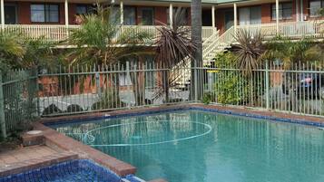A swimming pool with a tiled edge, surrounded by a fence, and adjacent to a building with multiple windows and balconies.
