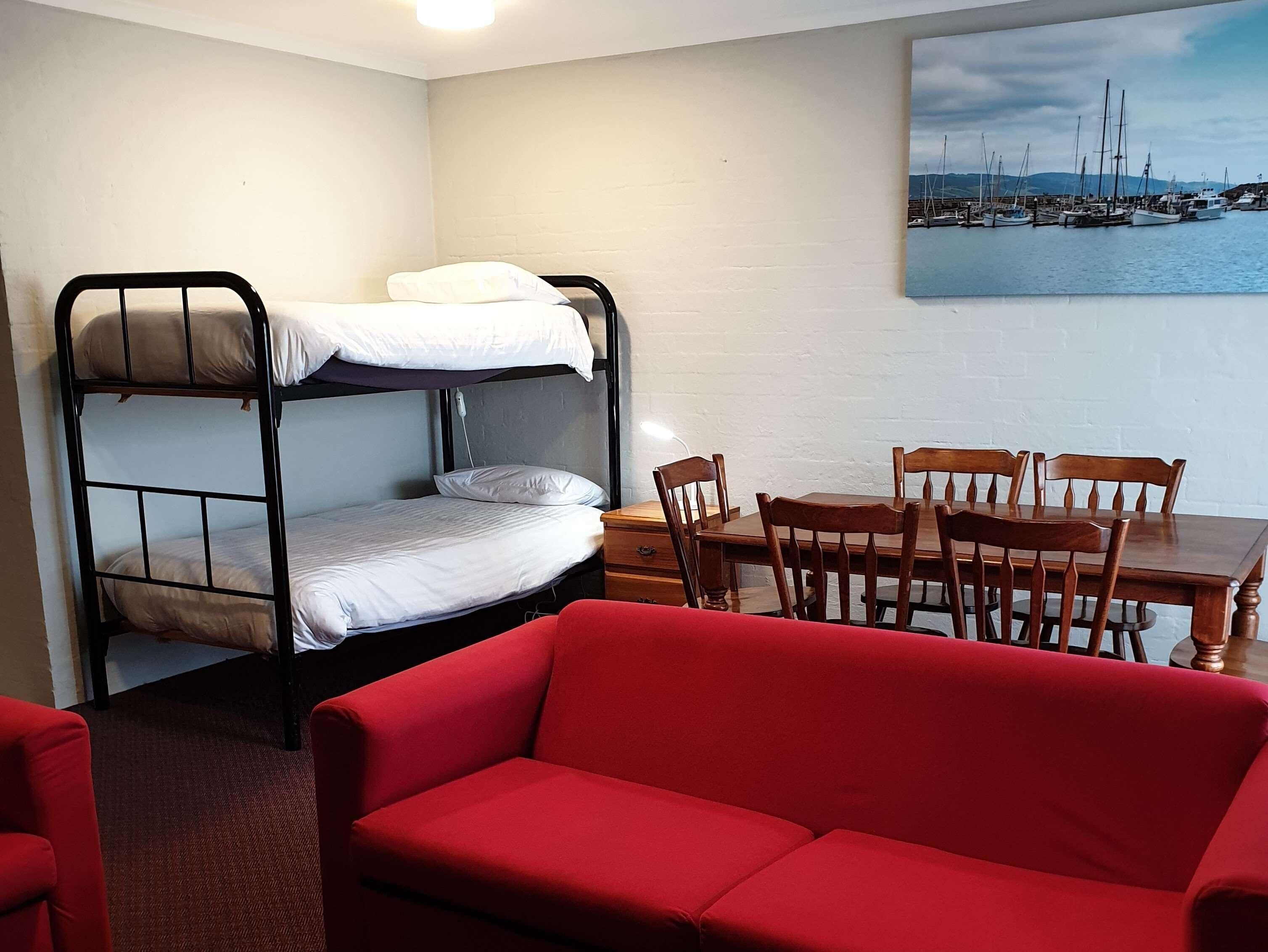 A room with a bunk bed, a wooden dining table with chairs, and a red sofa.