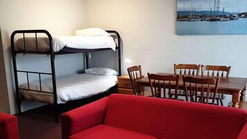 A room with a bunk bed, a wooden dining table with chairs, and a red sofa.