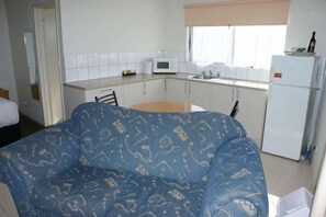 A compact kitchen with white cabinets, a microwave, a refrigerator, and a dining area with a table and chairs. - Apollo Bay Motel & Apartments (Apollo Bay)