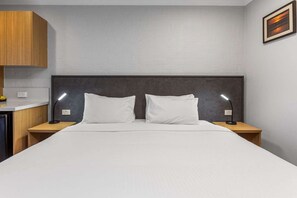 A bedroom with a large bed, two bedside lamps, a wooden headboard, and a wall-mounted picture. - Apollo Bay Motel & Apartments (Apollo Bay)