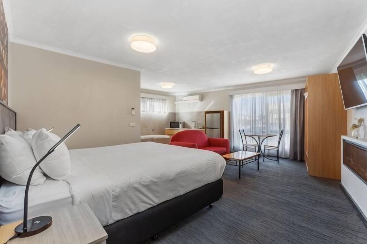 A hotel room with a bed, a desk, a chair, a TV, and a window.