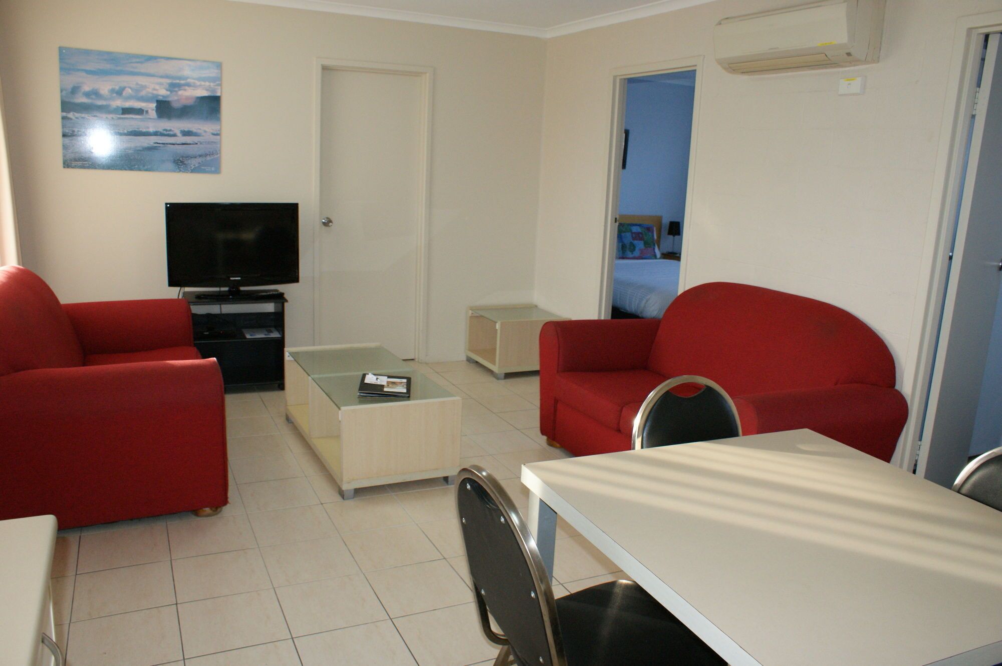 A compact living space with a television, red sofas, a small table, and a door leading to a bedroom.