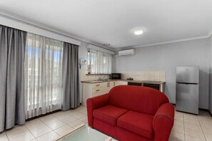 A modern living room with a red sofa, a kitchen area with a refrigerator, and a dining table. - Apollo Bay Motel & Apartments (Apollo Bay)