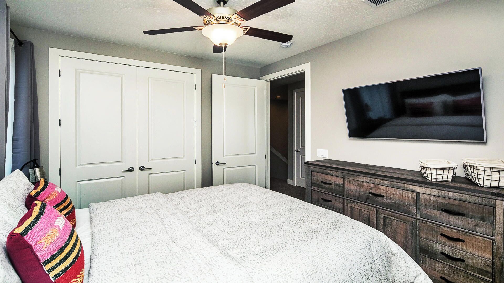Ein Schlafzimmer mit Bett, Schminktisch, Deckenventilator und Fernseher an der Wand.