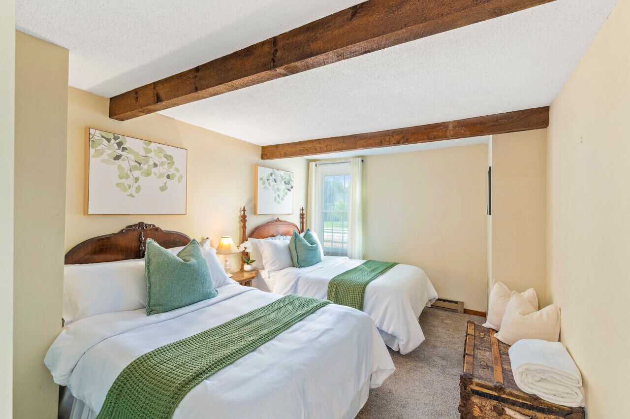 A hotel room with two beds, wooden beams on the ceiling, a window, and artwork on the walls.