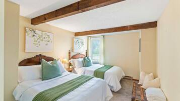 A hotel room with two beds, wooden beams on the ceiling, a window, and artwork on the walls.