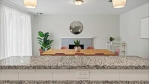 A modern kitchen with granite countertops, a central island, and a dining area with a long table and chairs. - Luxury Vacation Home with private pool. (Jacksonville)