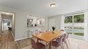 A spacious dining area with a wooden table and chairs, a kitchen in the background, and a view of a swimming pool. - Luxury Vacation Home with private pool. (Jacksonville)
