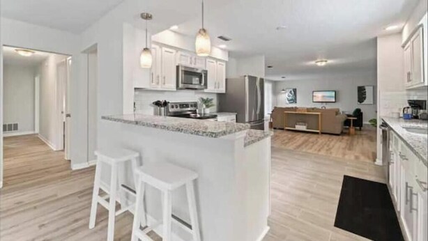 A modern kitchen with white cabinets, a central island with stools, and a dining area in the background. - Luxury Vacation Home with private pool. (Jacksonville)