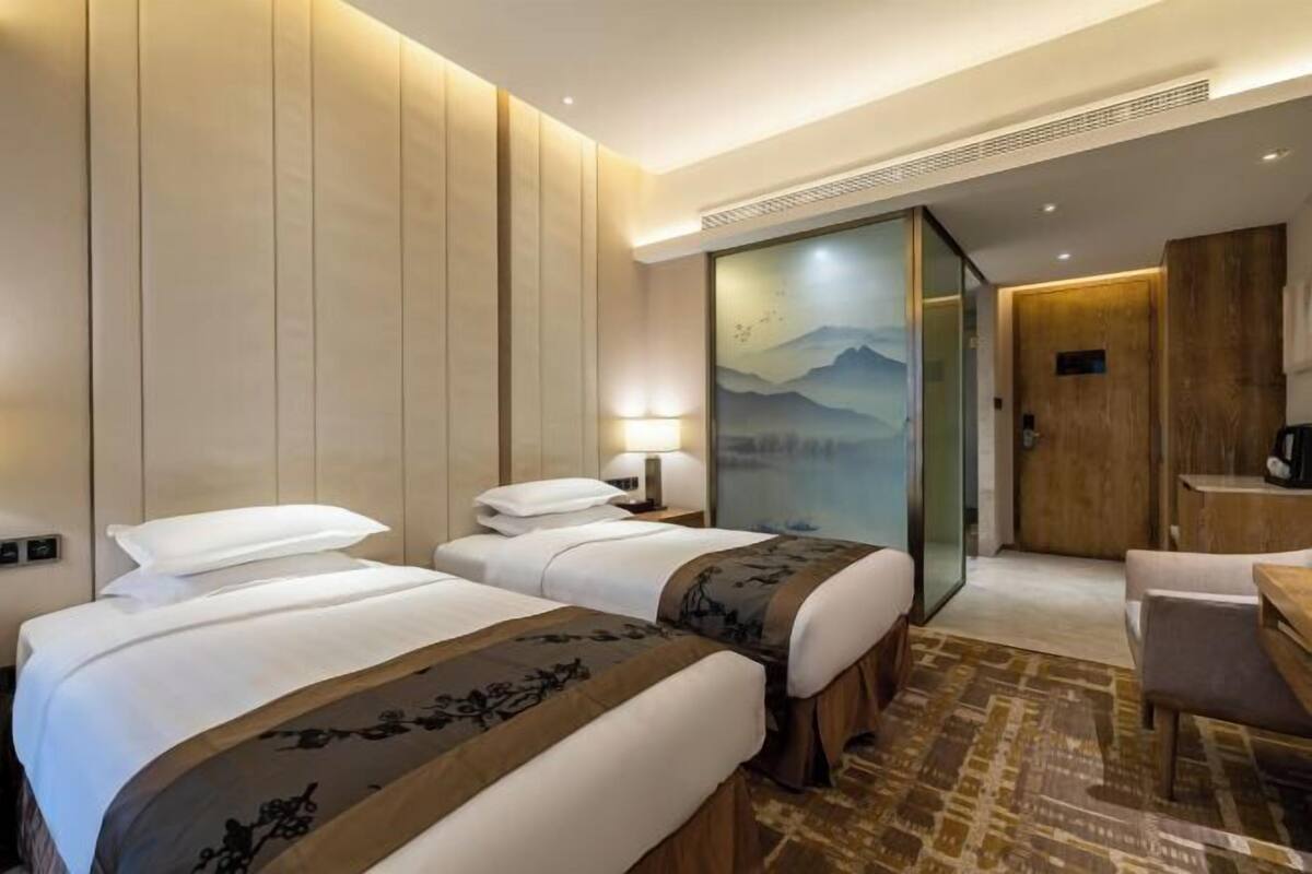 Habitación de hotel con dos camas, un escritorio y vista a montañas a través de un ventanal.