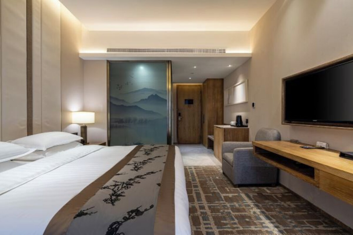 A hotel room with a bed, a desk, a chair, a television, and a door with a view of mountains.