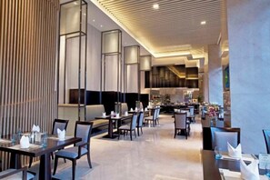 Een modern restaurant met hoge plafonds, inbouwverlichting en een combinatie van zitplaatsen, waaronder tafels en hoekbanken.