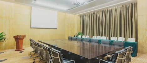 Un salón de conferencias con una larga mesa, sillas, un atril y una pantalla de proyector.
