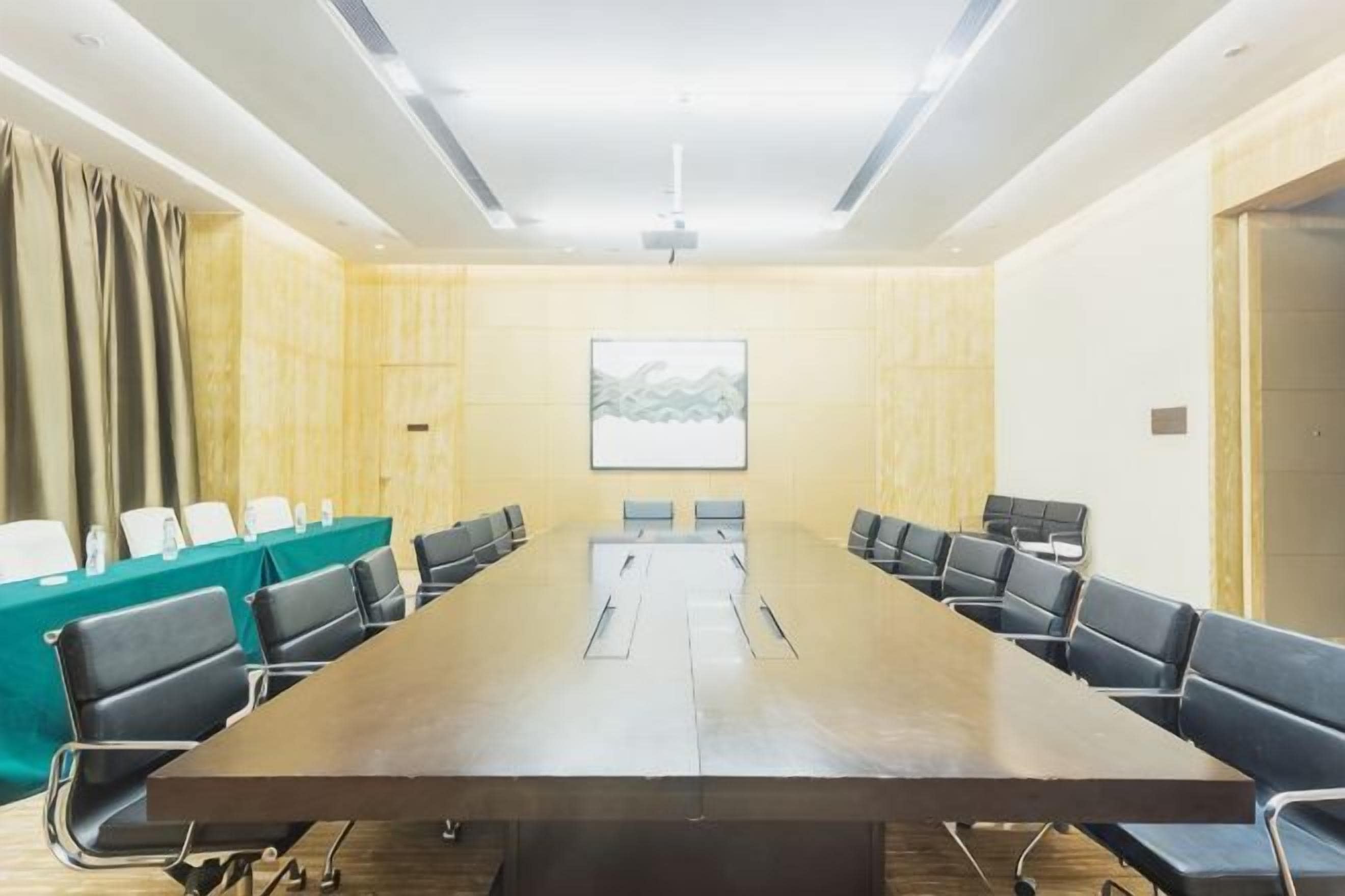 A conference room with a long table, chairs, a projector screen, and a green partition.