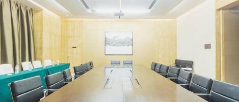 A conference room with a long table, chairs, a projector screen, and a green partition.