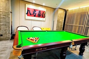 Een pooltafel met een groene viltbekleding en een witte poolbal in het midden, omringd door stoelen.