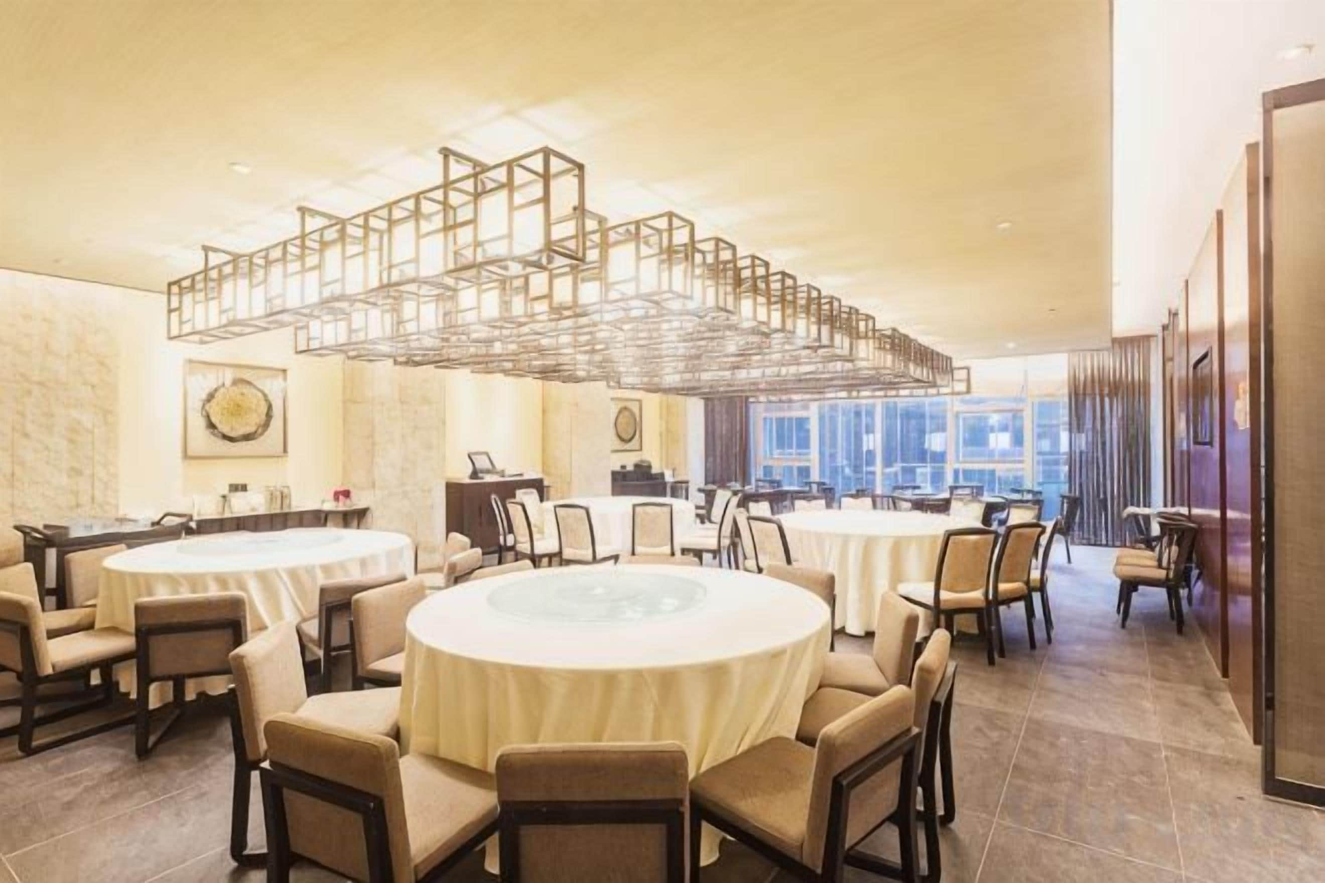 A hotel dining area with round tables, chairs, and a modern chandelier.