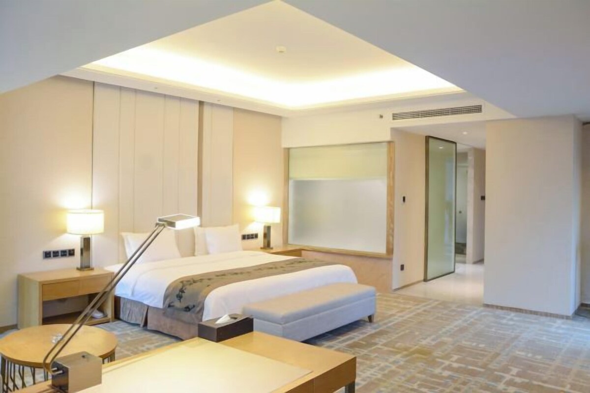 A modern hotel room with a large bed, bedside tables, a desk, and a chair.