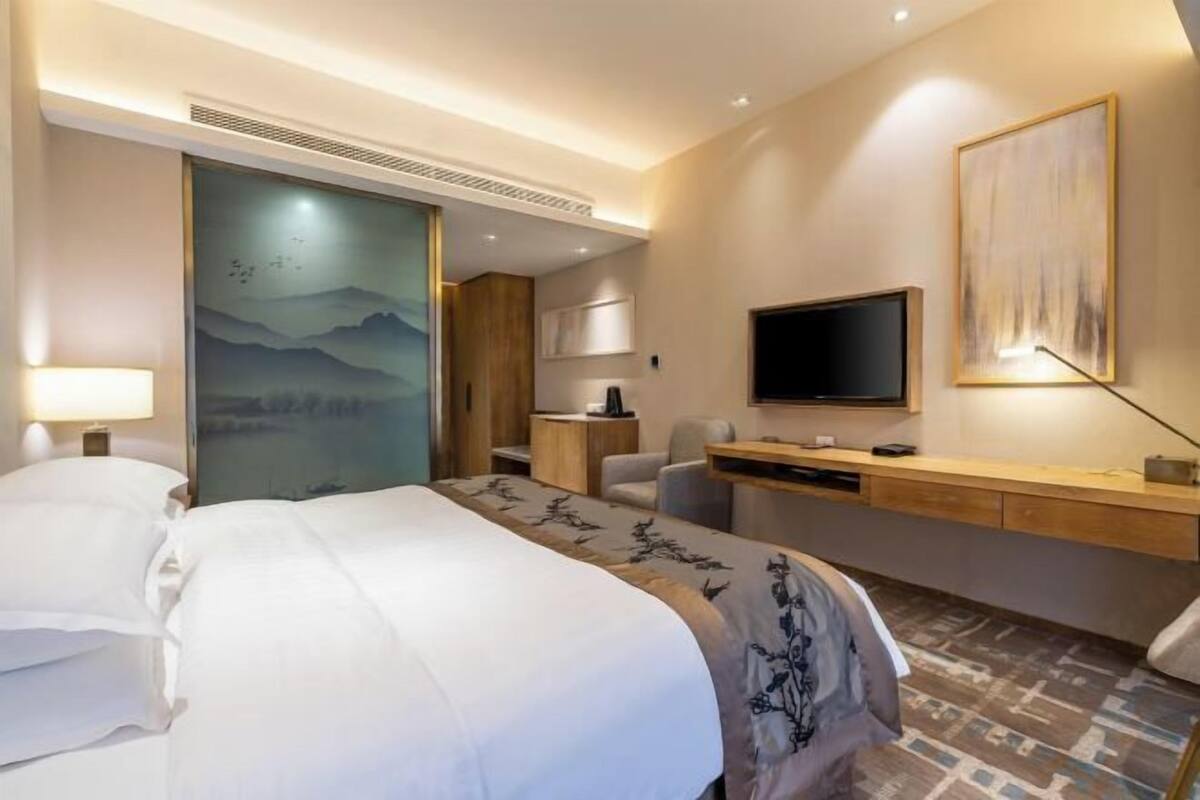 Habitación de hotel con cama, escritorio, silla, televisor y obra de arte en la pared.