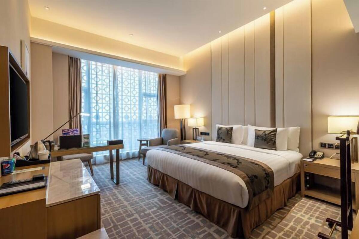 Habitación de hotel con una cama grande, un escritorio, un televisor y una ventana con vistas.