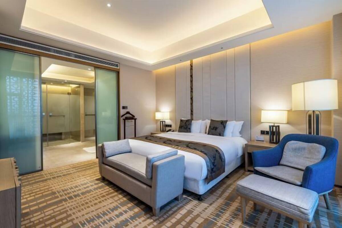 Una habitación de hotel moderna con una cama grande, un sofá, una silla y un panel de vidrio.