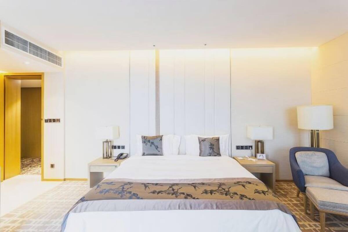 Una habitación de hotel con una cama grande, dos mesitas de noche, un escritorio, una silla y una lámpara.