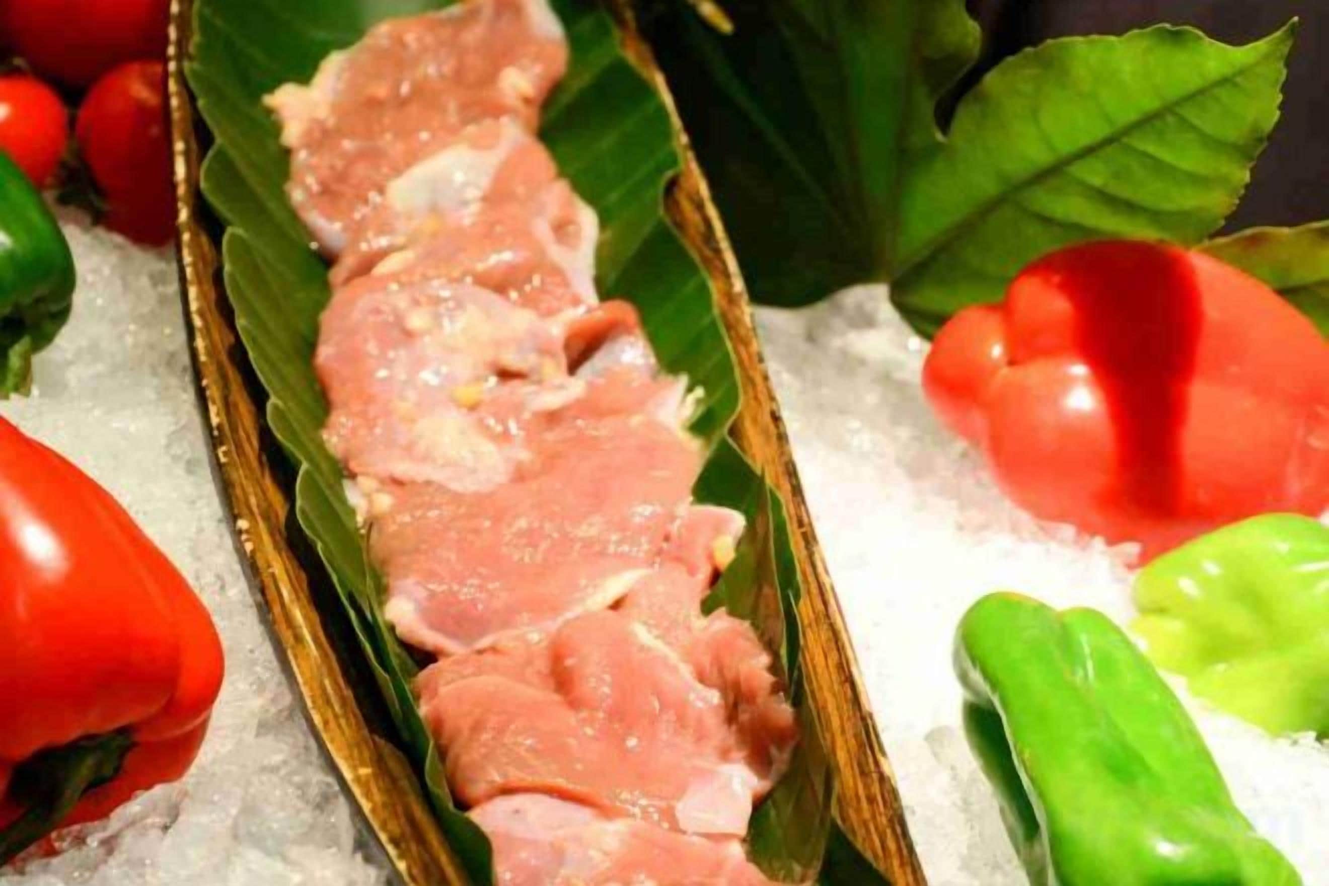 A tray of sliced meat on a bed of ice with cherry tomatoes and green peppers around it.