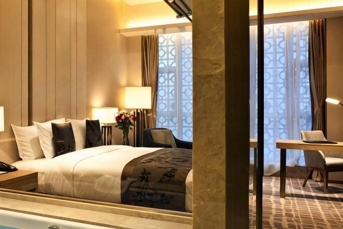 Habitación de hotel con cama, mesita de noche, lámpara, silla y vistas a través de una ventana con cortinas.